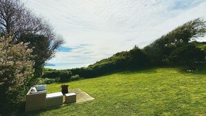 Ein sonniger, begrünteter Außenbereich mit Sitzgelegenheit und Blick auf das Meer.