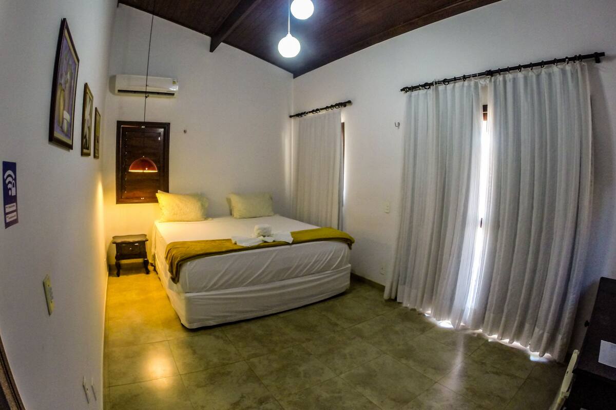 A bedroom with a bed, curtains, a ceiling light, and a wall-mounted air conditioner.