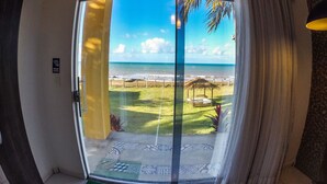 Ein Zimmer mit Glastür und Blick auf einen Strand, eine kleine Struktur mit Reetdach sowie ein Fliesenboden.
