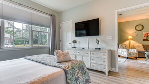 Ein Schlafzimmer mit Bett, Kommode, Fernseher und Blick ins Freie.