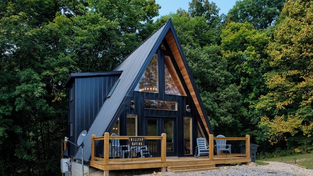 A modern cabin with a sloped roof, large windows, and a wooden deck with seating. - Tranquil retreat nestled in the breathtaking landscape of Hocking Hills. (McArthur)