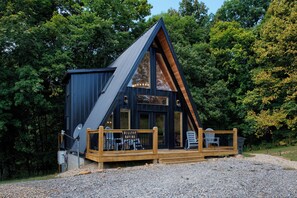 A modern cabin with a sloped roof, large windows, and a wooden deck with seating. - Tranquil retreat nestled in the breathtaking landscape of Hocking Hills. (McArthur)