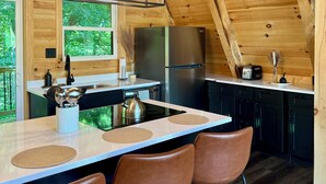 A modern kitchen with wooden beams, a central island with bar stools, stainless steel appliances, and a view of greenery outside. - Tranquil retreat nestled in the breathtaking landscape of Hocking Hills. (McArthur)