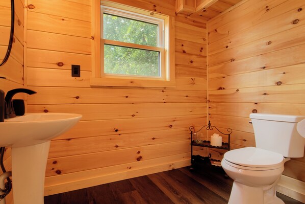 Un baño con paneles de madera, un lavamanos blanco, un inodoro y una ventana.