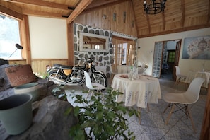 A rustic interior with a stone wall, wooden ceiling, a motorcycle, a dining table with chairs, and a Buddha painting. - Refugio Atreyu (Lo Barnechea)