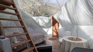 A cozy tented accommodation with a wooden ladder, a bed with a patterned blanket, a small table with a vase, and a chair. - Refugio Atreyu (Lo Barnechea)
