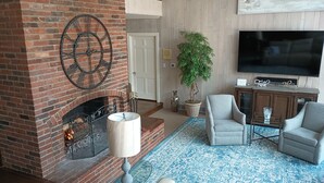 A living room with a brick fireplace, a television, two armchairs, a patterned rug, and a potted plant. - Beautiful and Scenic 6 bedrooms and 6 bathrooms large pool a hot tub 7000sqft (Prospect)