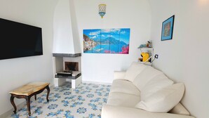 A living room with a fireplace, a sofa, a TV, and a painting of a coastal scene.