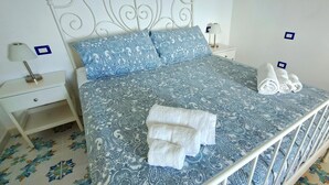 A neatly made bed with a patterned bedspread, two pillows, and rolled towels on the side.
