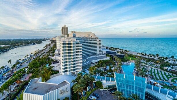 A coastal hotel with a large swimming pool, multiple high-rise buildings, and a view of the ocean. - Junior Suite Ocean View Floor Fontainebleau (Miami Beach)