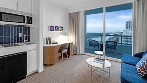 A modern hotel room with a kitchenette, a dining area, and a balcony with a city view. - Junior Suite Ocean View Floor Fontainebleau (Miami Beach)