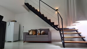 Een moderne woonkamer met een grijze bank, een witte koelkast en een zwarte trap met een leuning.