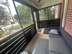 Un espacio al aire libre techado con un banco y un banco acolchado, un felpudo y vistas a la calle y al follaje.