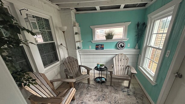 A cozy room with two wooden Adirondack chairs, a small round table, and a window with a plant on the sill. - 6 Block to oceanfront and in the center of the vibe district! (Virginia Beach)