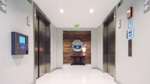 A modern elevator lobby with a digital control panel, a wooden accent wall, and a polished floor.