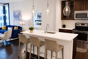 A modern kitchen with a central island, stainless steel appliances, and pendant lighting. - Blue Luxe | Balcony View | Pool | Modern Amenities (Atlanta)