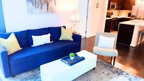 A modern living room with a blue sofa, a white coffee table, and a grey armchair.