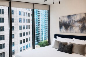 A modern hotel room with a large bed, a view of a high-rise building, and a painting on the wall. - Blue Luxe | Balcony View | Pool | Modern Amenities (Atlanta)