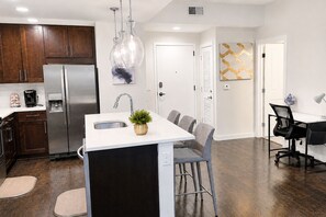 A modern kitchen with a central island, stainless steel appliances, and a dining area with a white table and grey chairs.