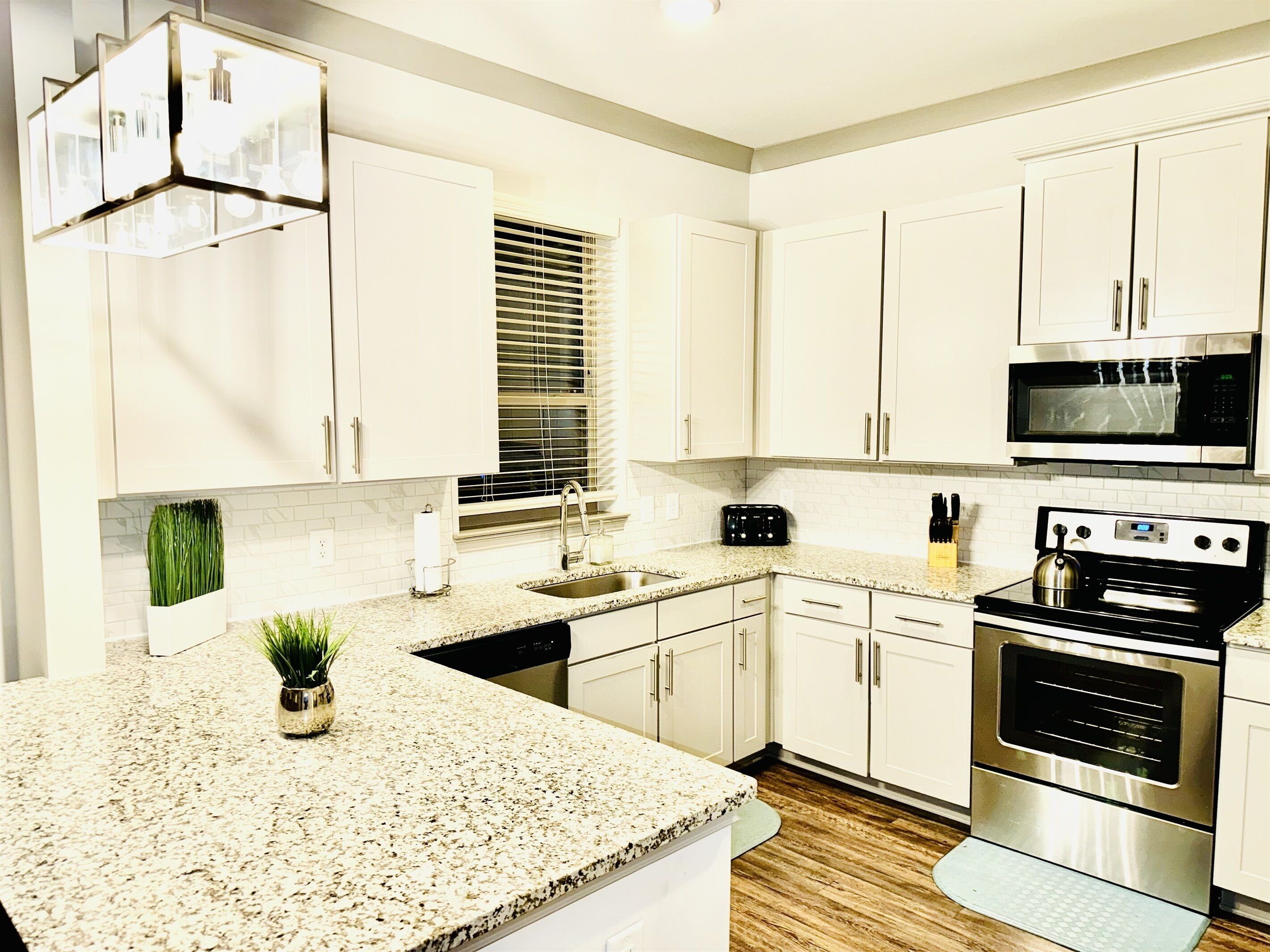 A modern kitchen with white cabinets, a granite countertop, a stainless steel stove, and a microwave.
