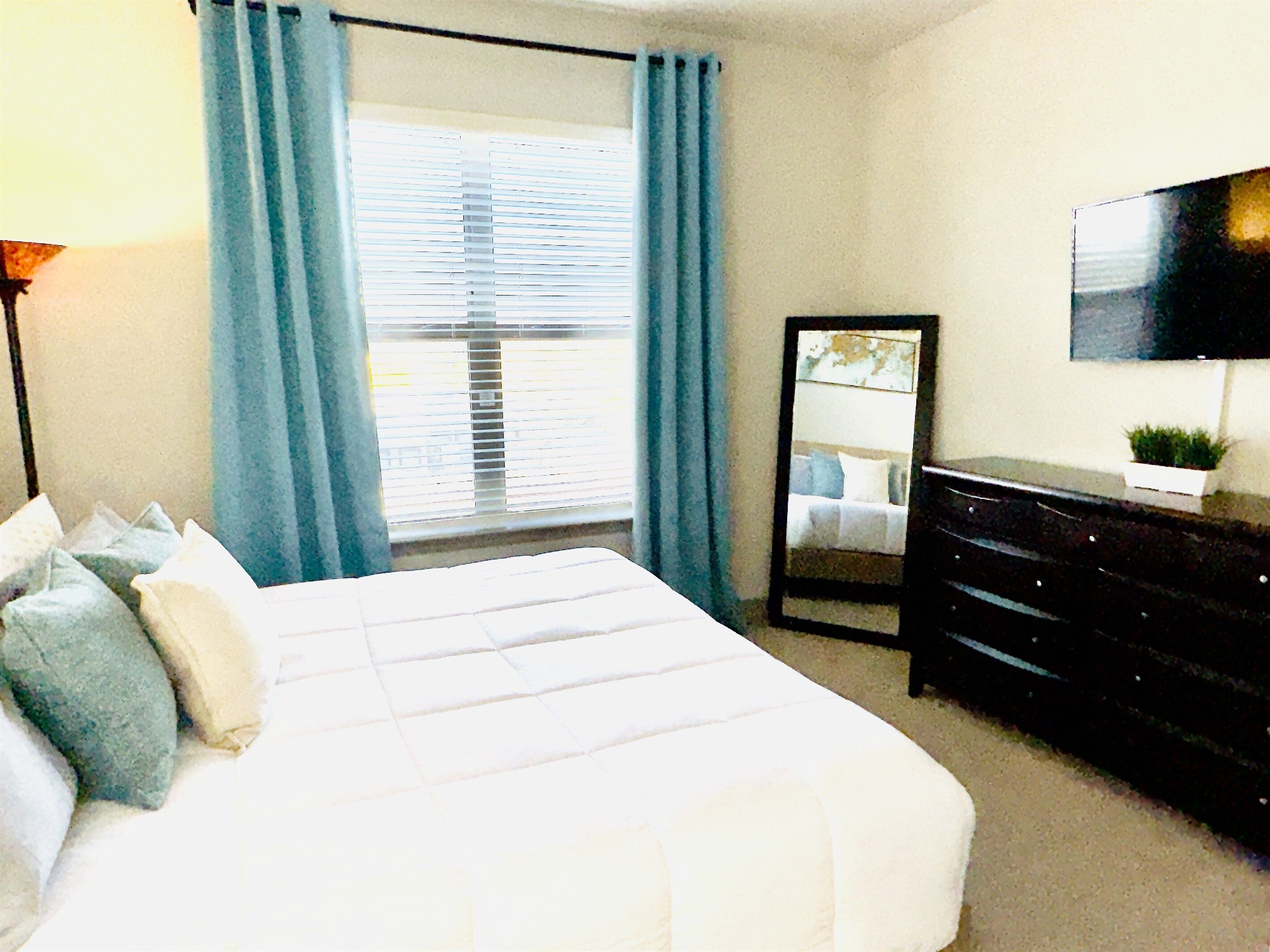 A bedroom with a bed, a dresser, a mirror, and a TV on the wall.