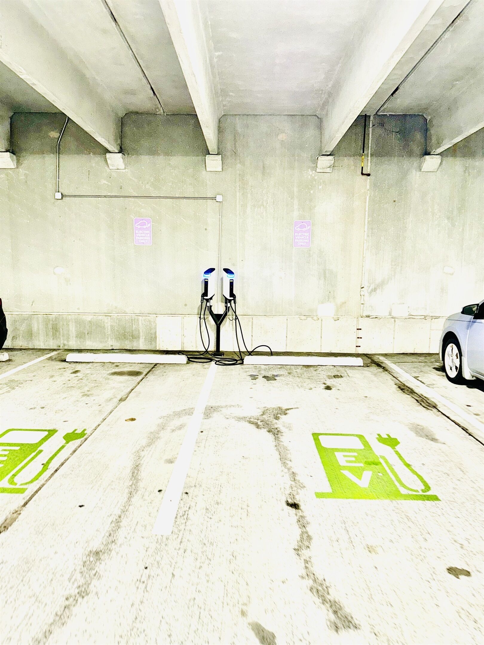 An indoor parking area with electric vehicle charging stations, marked parking spaces, and concrete walls.