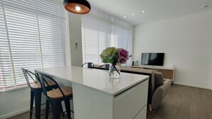 A modern kitchen with a central island, white cabinetry, and a dining area with two chairs. - AL.Fredos 1| Mindelo | Beachfront (Mindelo)