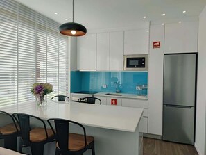A modern kitchen with white cabinets, a blue backsplash, a stainless steel refrigerator, and a pendant light.