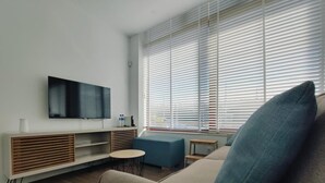 A modern living room with a flat-screen TV, a sofa, a small round table, and a blue armchair. - AL.Fredos 2| Mindelo | Beachfront (Mindelo)