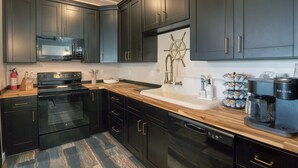 A modern kitchen with dark cabinetry, a stainless steel range, a double sink, and a coffee maker. - Camp Conex a Shipping Container in Shell Beach, LA (St. Bernard Parish)