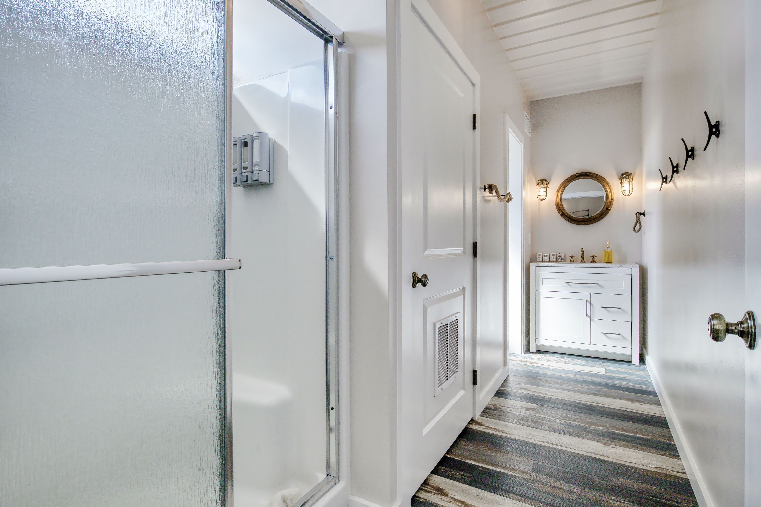 Un couloir aux murs blancs, avec un plancher en bois, une porte blanche et un meuble blanc doté de tiroirs.