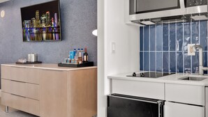 A modern kitchen with a built-in microwave, oven, and sink. There is a wooden cabinet with drawers and a countertop with a few items on it. A flat-screen TV is mounted on the wall above the cabinet.