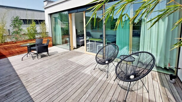 A modern outdoor deck with a wooden floor, glass sliding doors, and two black wire chairs. - ROSE valley -modern rooms and apartments (Ljubljana)