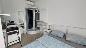 A modern hotel room with a bed, a desk, a chair, a shower, and a small table with a lamp. - ROSE valley -modern rooms and apartments (Ljubljana)