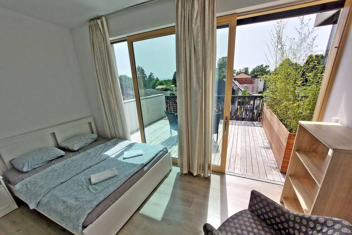 A bedroom with a large bed, a small sofa, and a balcony with a wooden deck.