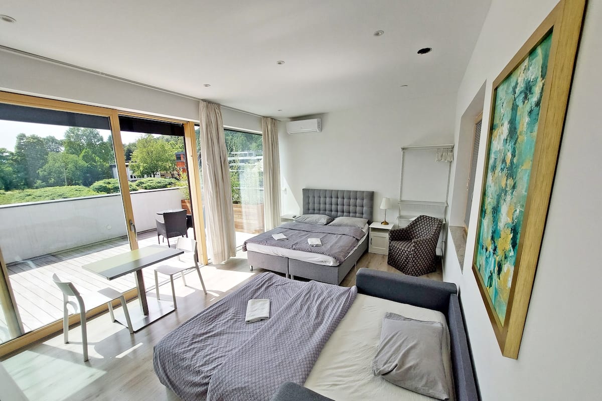 A modern bedroom with a large bed, a sofa, and a balcony with a table and chairs.