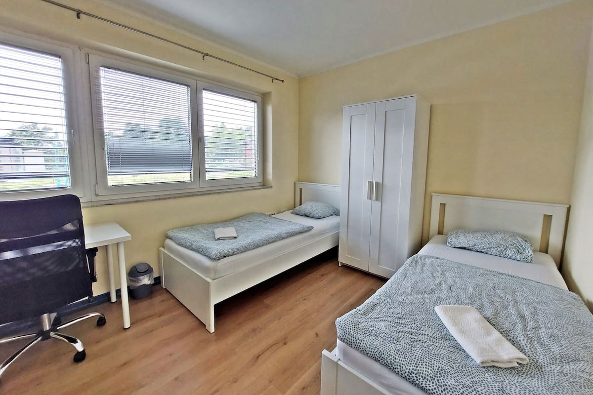A bedroom with two single beds, a white wardrobe, a desk, and a chair.