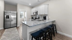 A modern kitchen with a stainless steel refrigerator, a microwave, an oven, and a sink. There are bar stools at the island and a patterned rug on the floor. - Branson Beauty! 4brm condo! Central Location (Branson)