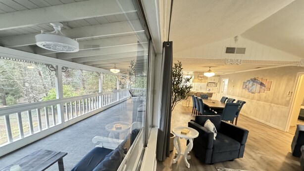 A modern living room with a large window, a dining area, and a kitchen visible through the glass wall.