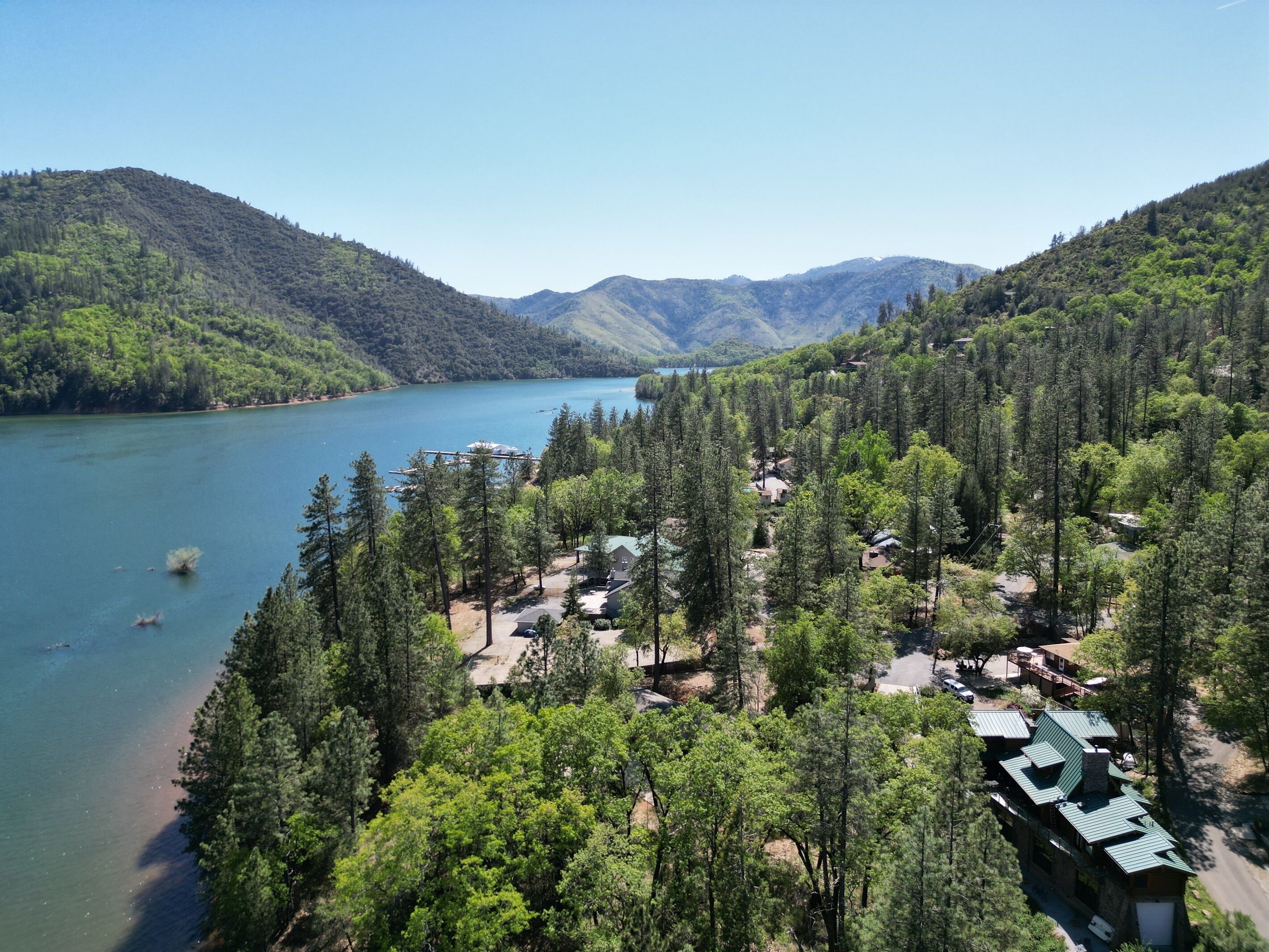 A lakeside lodge surrounded by dense forest, with a clear view of the lake and distant mountains.