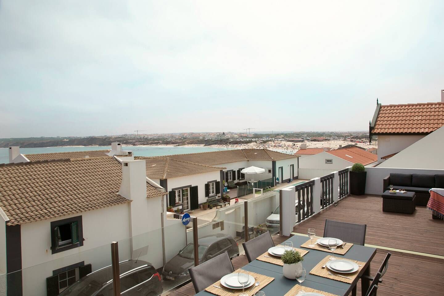 A rooftop terrace with a dining table set for two, overlooking a beach and cityscape.