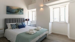 Une chambre moderne avec un grand lit, une vue sur la mer par la fenêtre et un tableau représentant une vague accroché au mur.