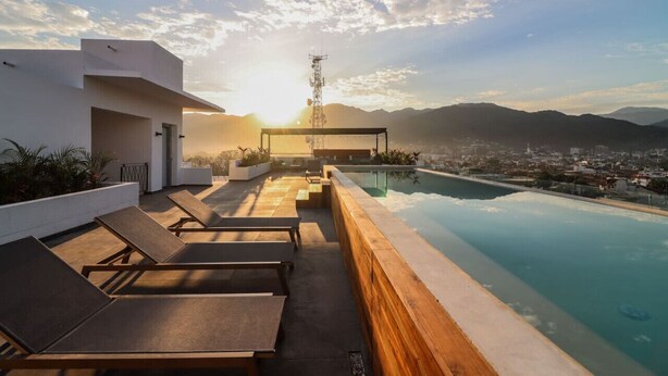 A rooftop pool area with lounge chairs and a view of the city and mountains.