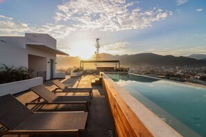 Zona de piscina en la azotea con sillones y vistas a la ciudad y montañas.
