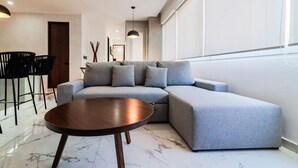A modern living room with a sectional sofa, a round wooden coffee table, and a dining area with chairs and a table.
