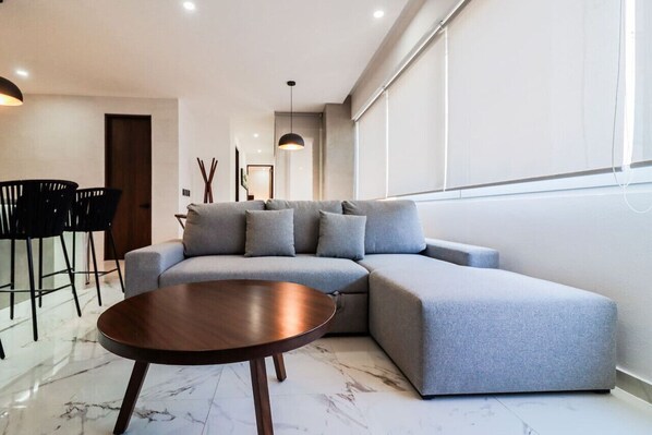 Una sala de estar moderna con un sofá modular, una mesa de centro redonda de madera, y un comedor con sillas y una mesa.