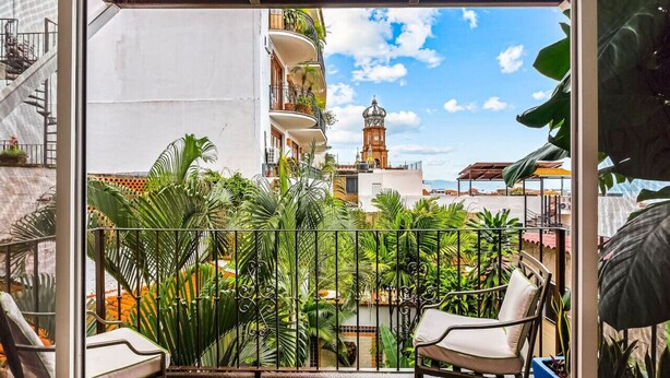 Een balkon met uitzicht op een toren en weelderige begroeiing.