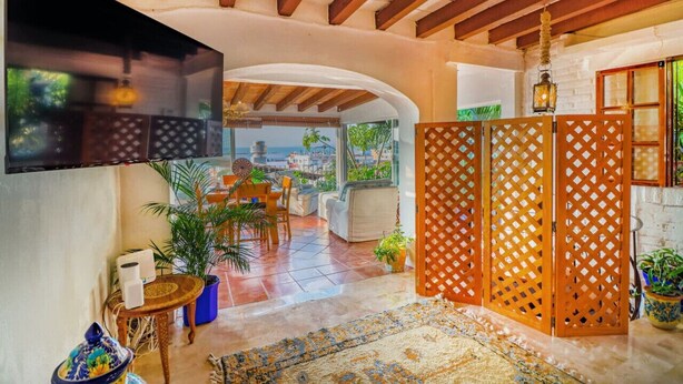 A spacious living area with a TV mounted on the wall, a wooden ceiling, and a view of the outdoors. - Studio La Vista – Stunning Views in the Heart of Puerto Vallarta (Puerto Vallarta)