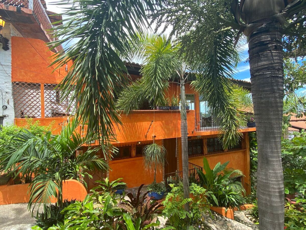 Un edificio a più piani con pareti arancioni e balconi, immerso nel verde e circondato da palme.