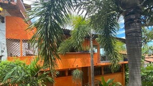 A multi-story building with orange walls and balconies, surrounded by lush greenery and palm trees. - Studio Romantique – Your Tropical Hideaway in Historic Puerto Vallarta (Puerto Vallarta)